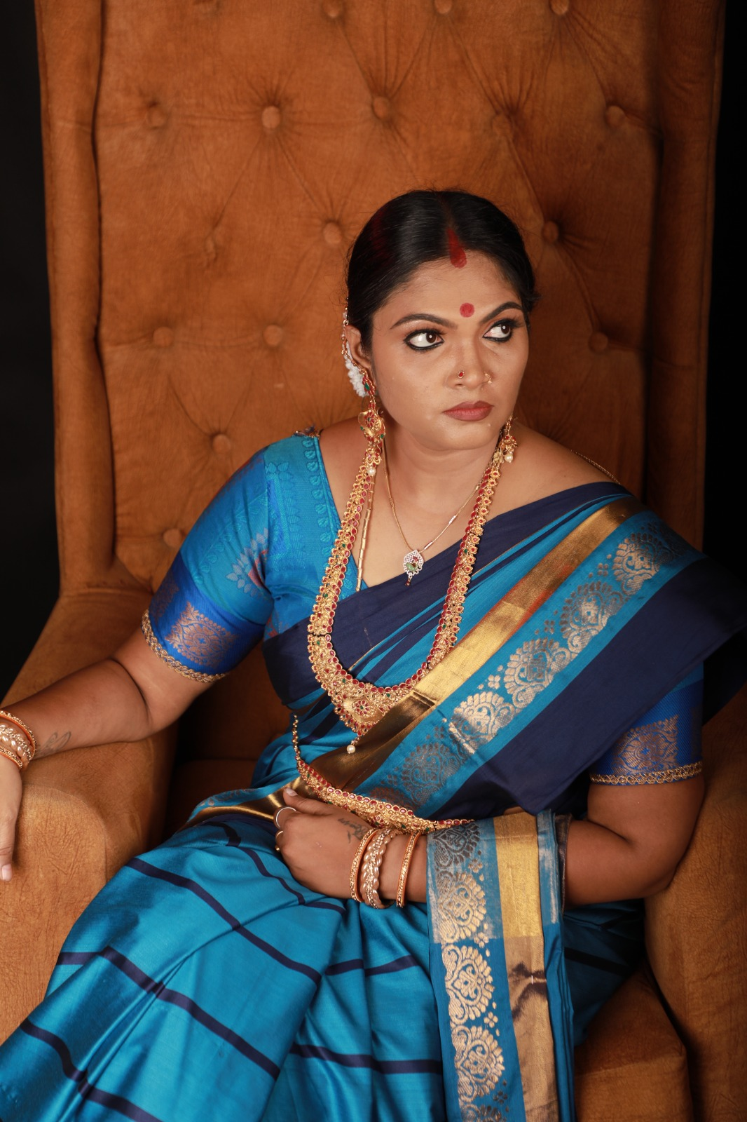 Woman wearing a royal blue silk saree with a gold border, traditional gold jewellery, red bindi, and classic South Indian makeup