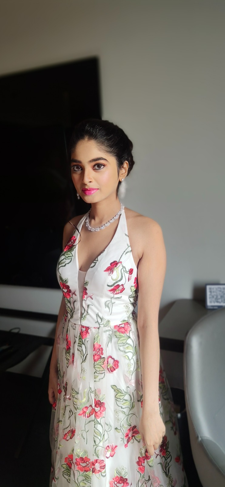 Woman wearing a white floral halter-neck gown with pink rose prints, a silver necklace, and elegant soft glam makeup