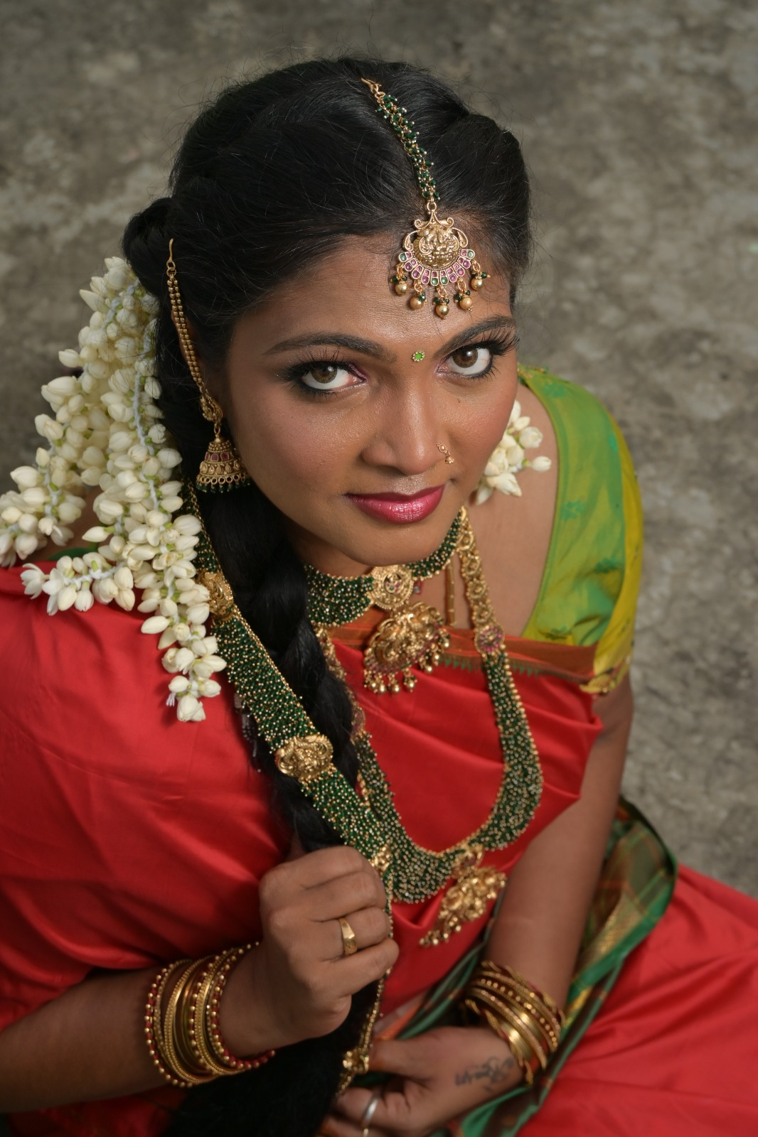 South Indian bride wearing a red silk saree with a green blouse, traditional gold temple jewellery, jasmine flowers, and elegant bridal makeup