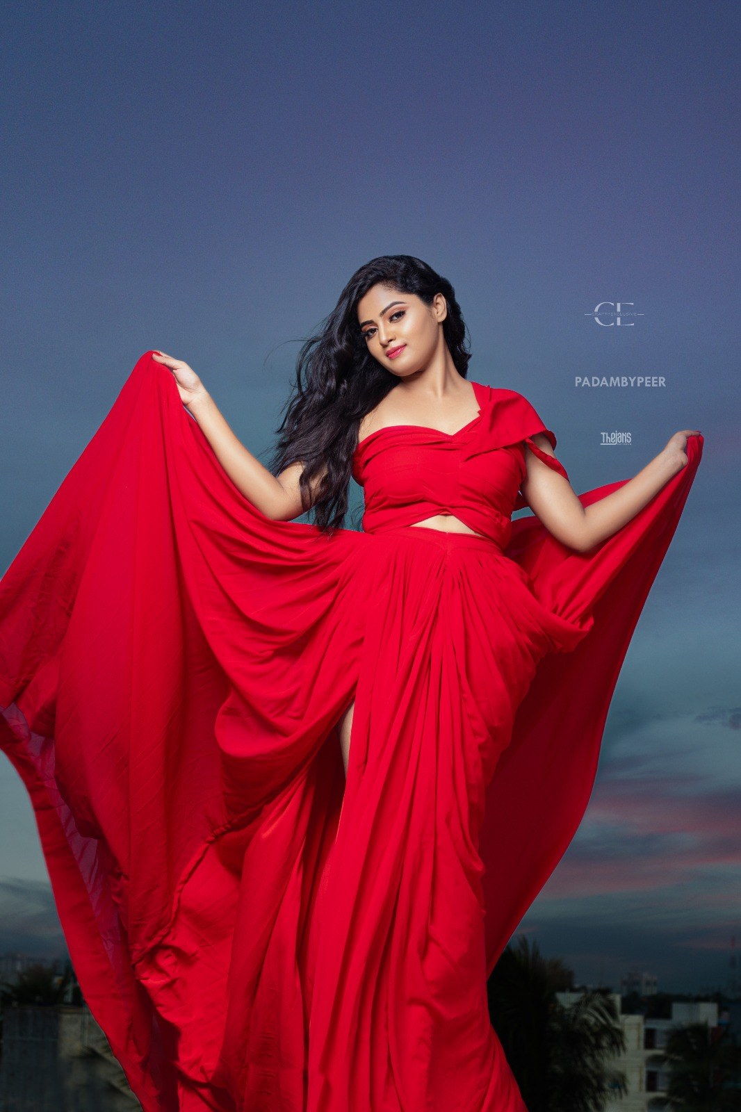 Woman in a flowing red gown posing against a blue-grey background