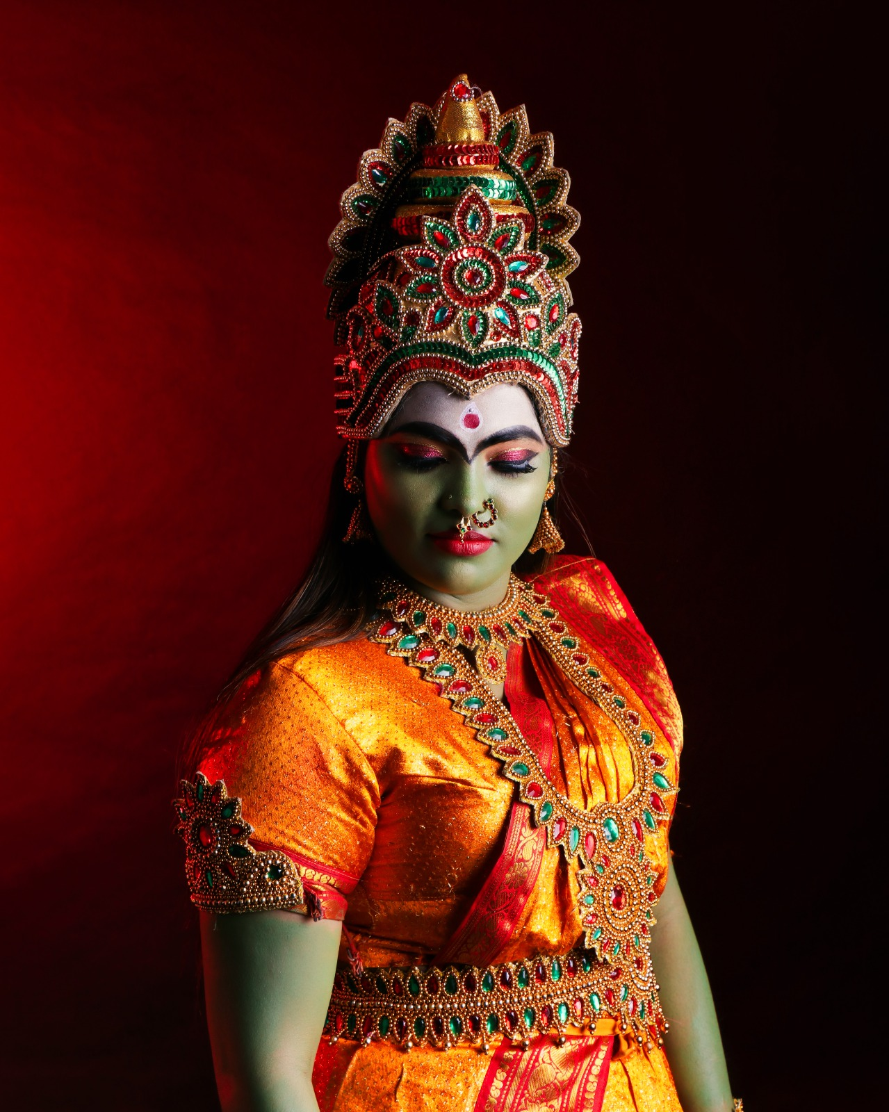 Woman dressed as Goddess Kali in an ornate traditional crown, red and gold costume, temple jewellery, and dramatic devotional makeup