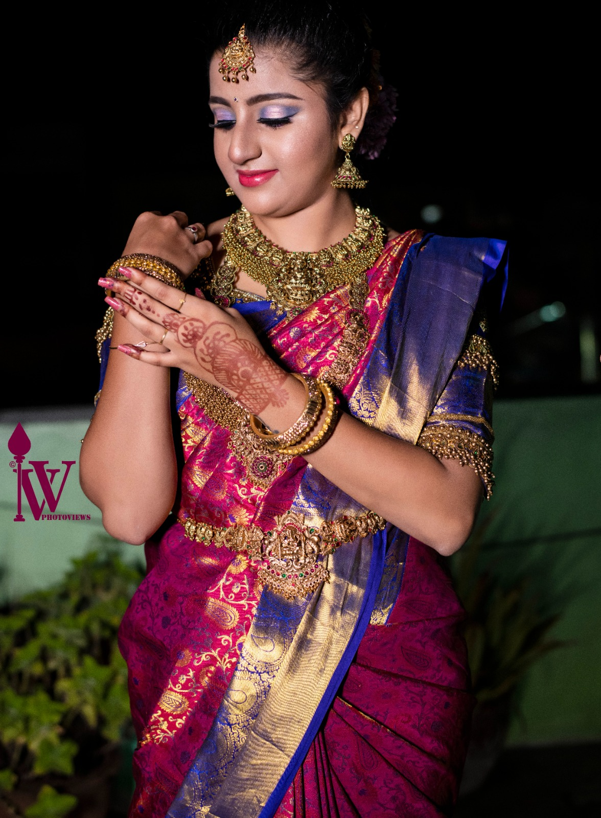 South Indian bride wearing a magenta and royal blue silk saree with a gold border, traditional temple jewellery, bridal mehndi, and elegant eye makeup