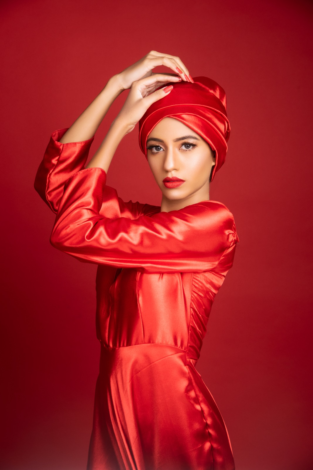 Woman in a luxurious red satin outfit and matching headwrap against a red background