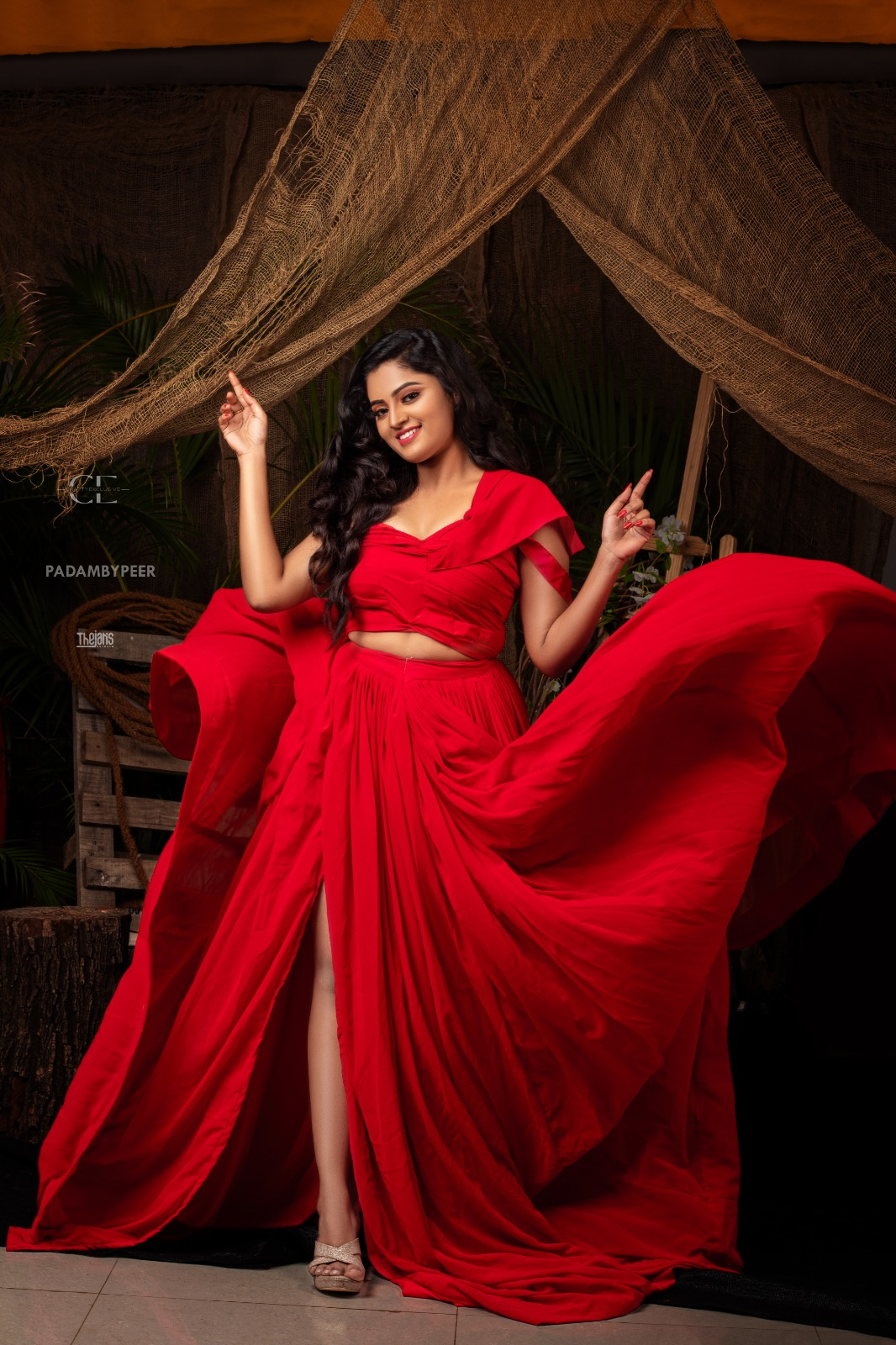 Woman wearing a flowing red gown with long wavy hair in a rustic outdoor studio setting