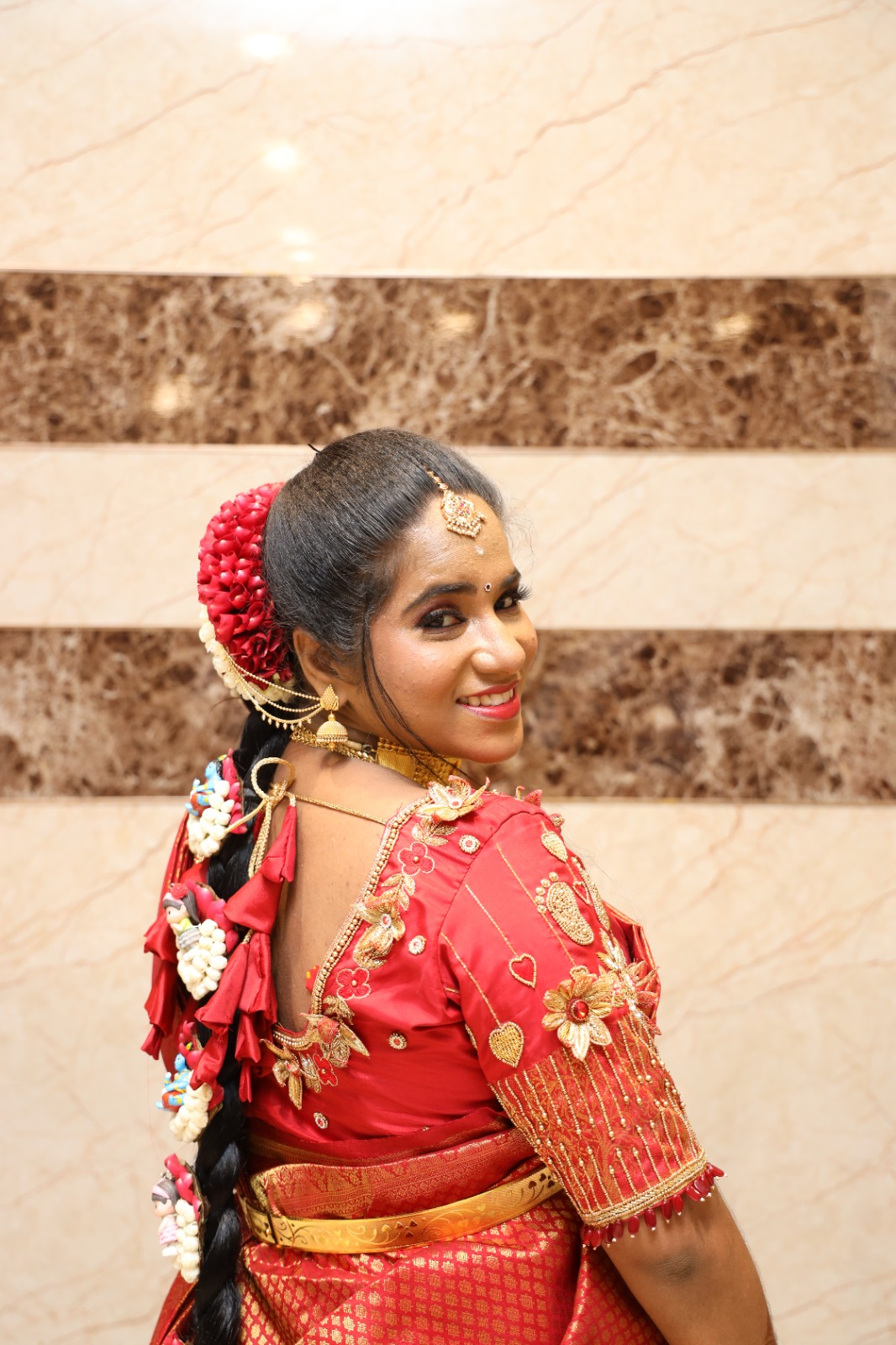 South Indian bride in a red and gold silk saree with traditional gold jewellery, a decorated jasmine and rose braid, and elegant bridal makeup